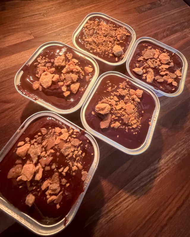 Five Butterfinger-topped brownie tins arranged on a wooden board